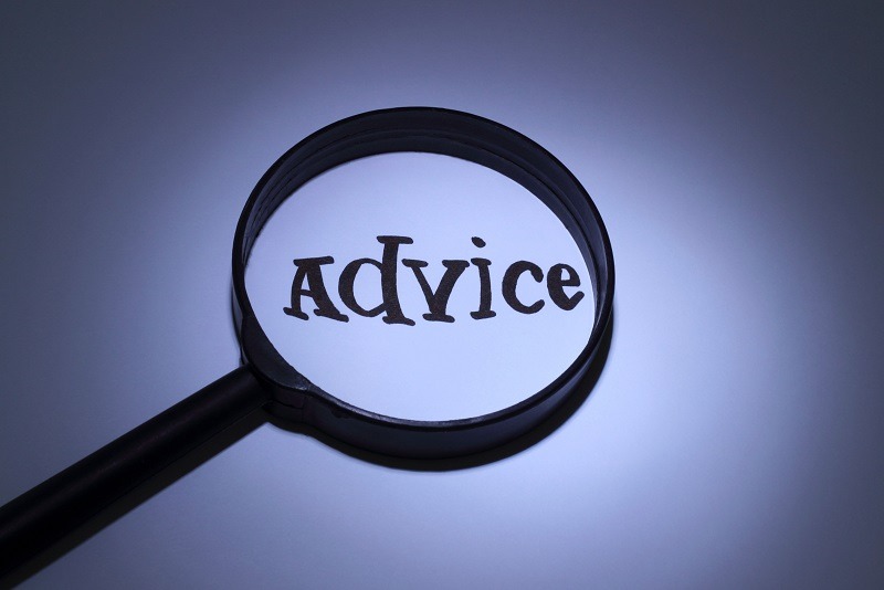 A magnifying glass enlarges the word advice written in bold letters on a white surface, emphasizing the concept of seeking or giving guidance.